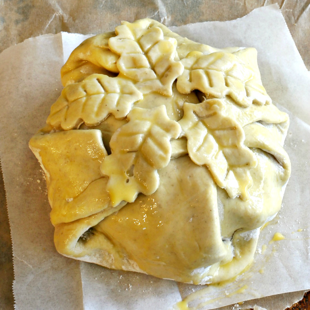 photo of brie wrapped with puff pastry dough brushed with egg and topped with leaf dough cut outs