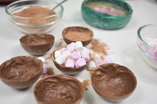 filled hot chocolate bombs on a white counter with hot cocoa mix and mini marshmallows in bowls in the background 