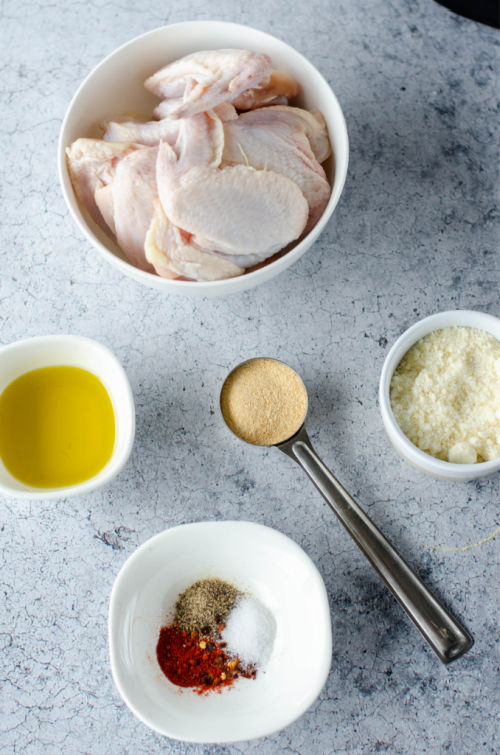 ingredients for garlic parmesan wings in separate bowls on a light blue kitchen counter