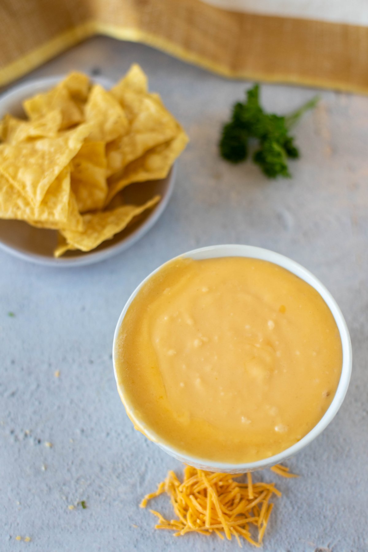 A bowl of cheese sauce next to a bowl of chips on a counter